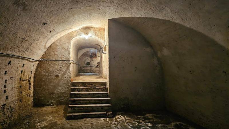 Historischer Kellerraum mit Gewölbedecke, Steintreppen und dunkler Atmosphäre.