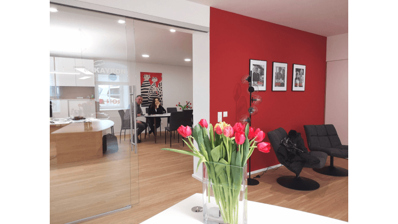 Moderner Empfangsbereich mit roten Wänden, Holzboden und Blick in ein offenes Büro.