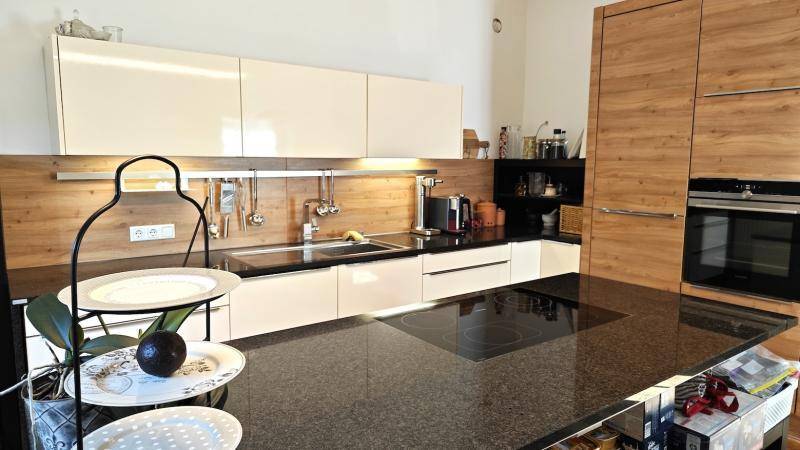 Moderne Küche mit cremefarbenen Hochglanzschränken, dunkler Arbeitsplatte und Einbaugeräten.