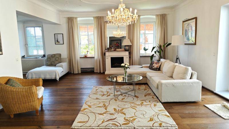 Elegantes Wohnzimmer mit Kronleuchter, Kamin, Parkettboden und großen Fenstern.