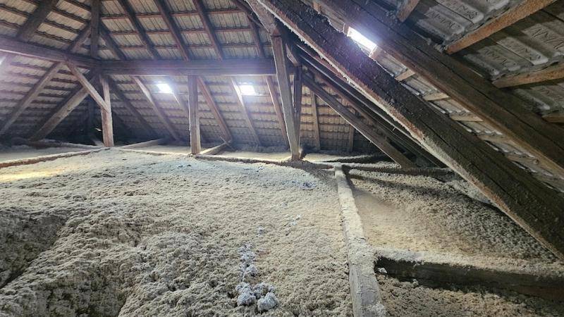 Dachboden mit sichtbaren Holzbalken, Dämmmaterial und Dachfenstern.