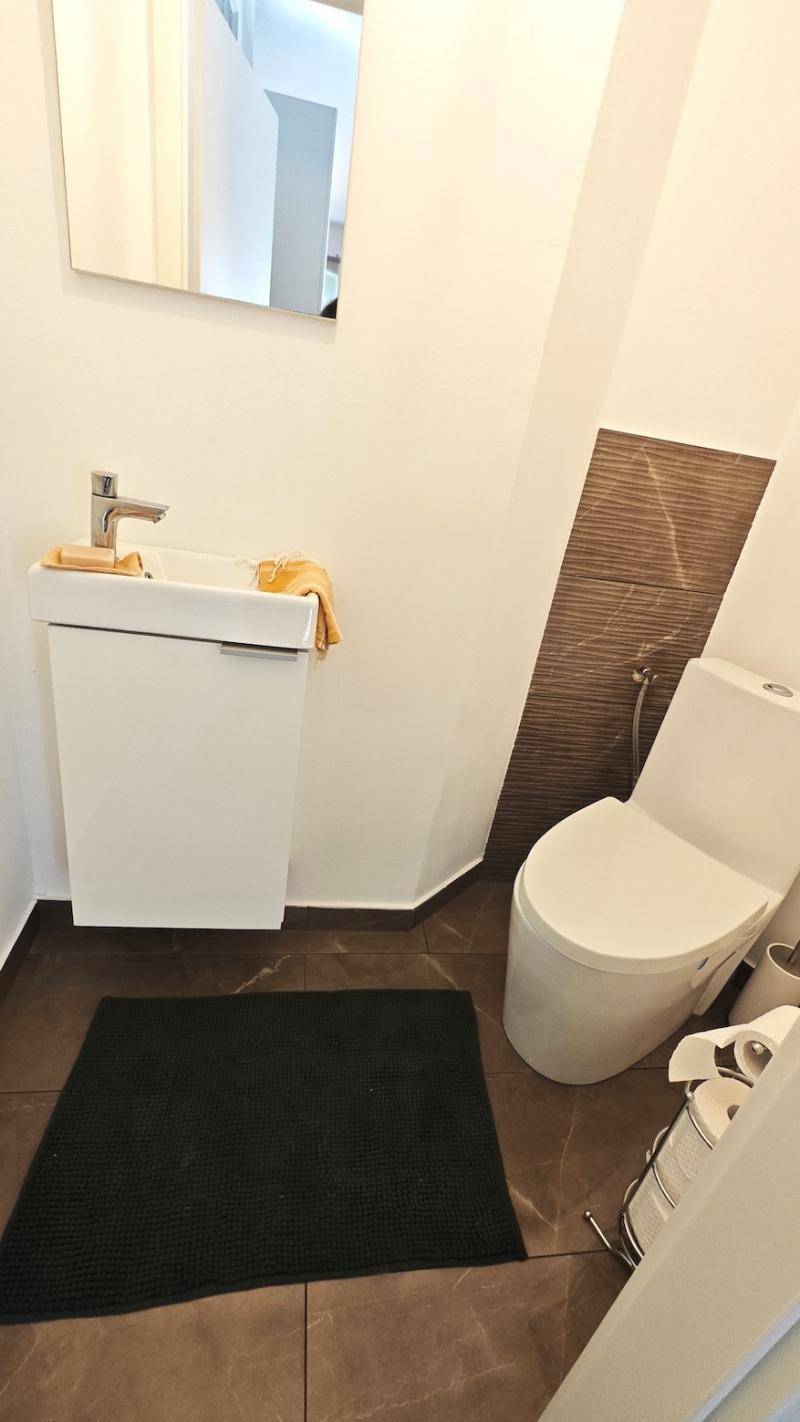 Kleines Gäste-WC mit modernem Waschbecken, Wand-WC und braunen Fliesen.