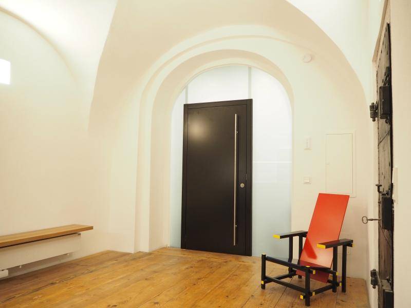 Heller Flur mit Gewölbedecke, Holzboden und moderner schwarzer Eingangstür.