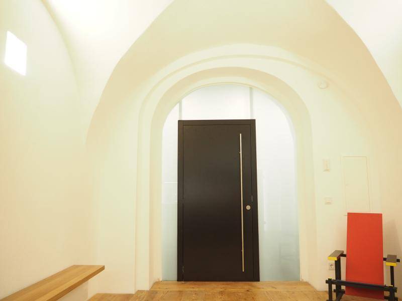 Heller Flur mit Gewölbedecke, Holzboden und moderner schwarzer Eingangstür, minimalistisch.
