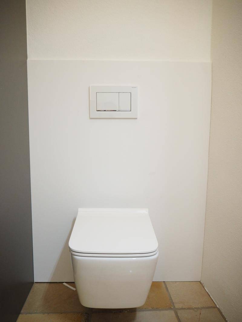 Modernes Wand-WC mit weißer Verkleidung und Fliesenboden.