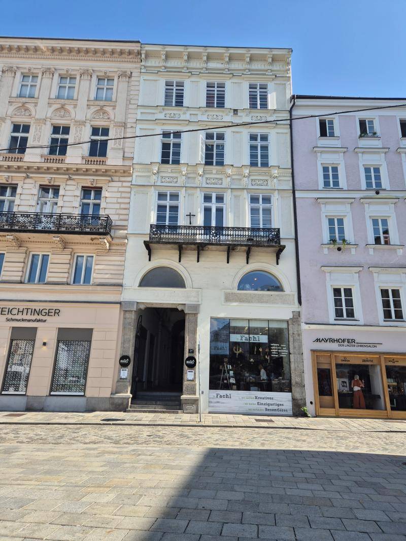 Historische Gebäudefassade mit mehreren Stockwerken, Geschäften im Erdgeschoss und Balkonen.