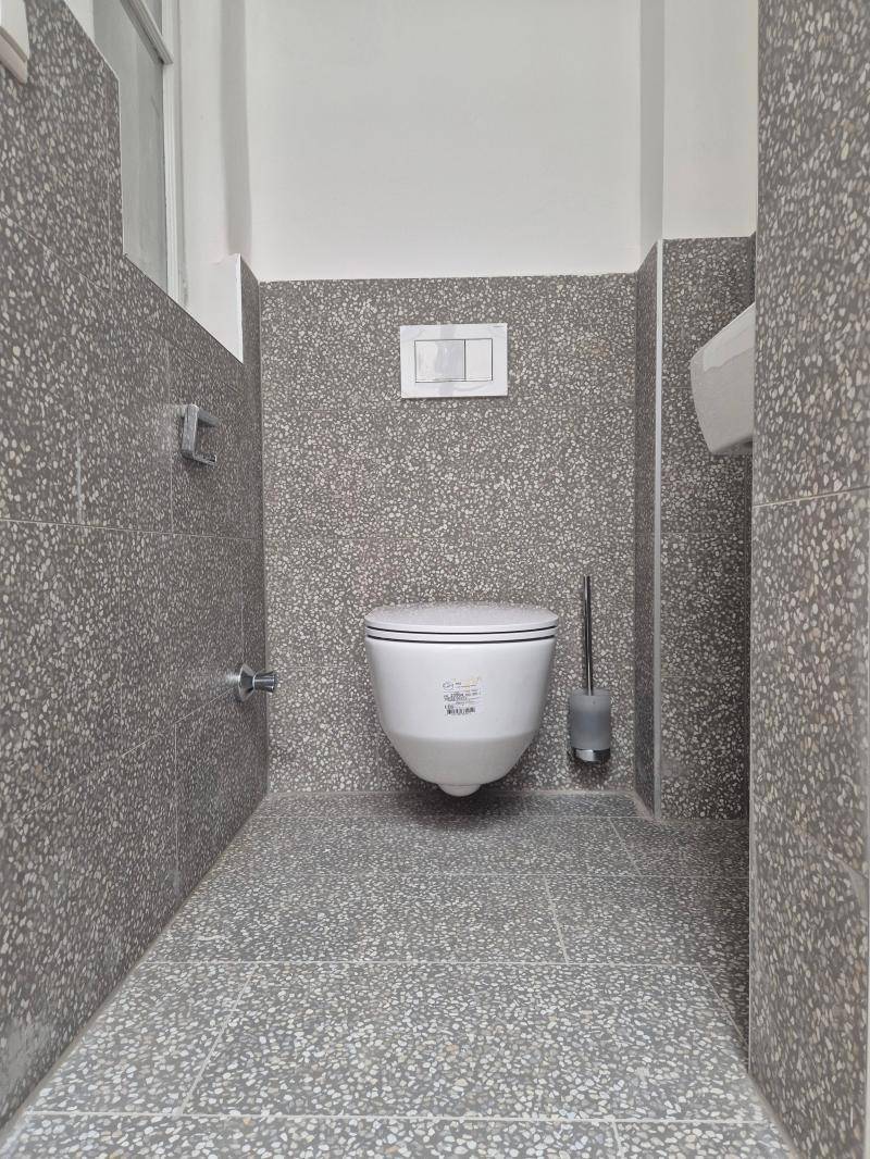 Kleine Gästetoilette mit grau gesprenkelten Fliesen an Boden und Wänden sowie wandhängendem WC.