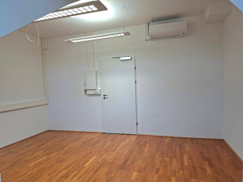 Leerer Raum mit Holzparkett, weißer Tür und installierter Klimaanlage an der Wand.