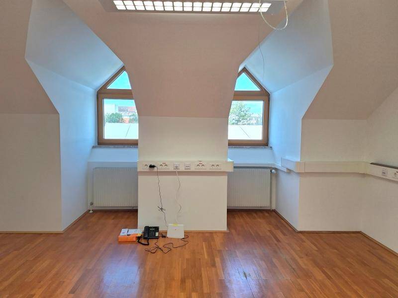 Geräumiger Dachraum mit zwei Fenstern, Holzparkett und schrägen Decken, ideal für ein Büro.
