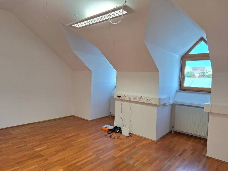 Heller Dachraum mit Holzfußboden, schrägen Wänden und einem Fenster, bereit zur Nutzung.