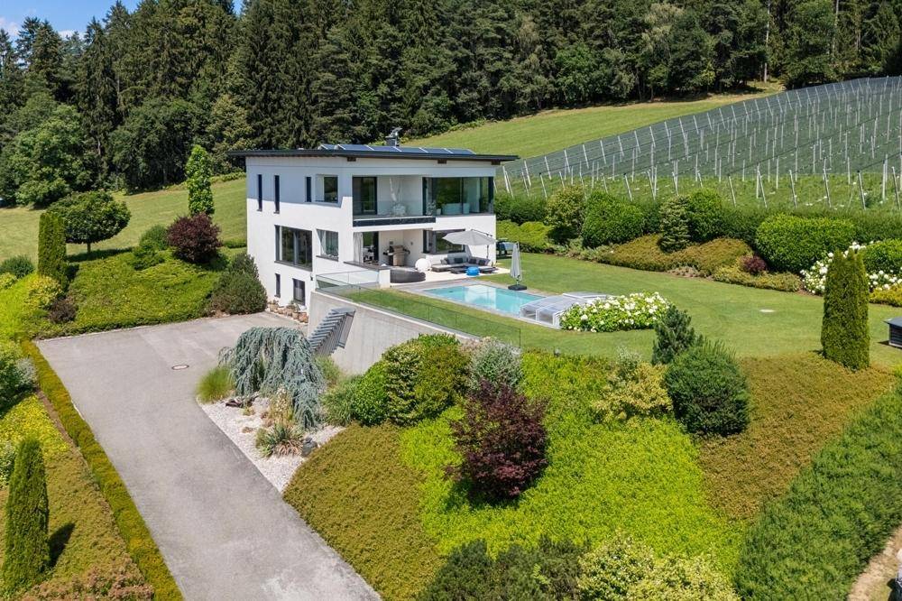 Luftaufnahme einer modernen Villa mit weitläufigem Grundstück, Pool und umgebender Naturlandschaft.