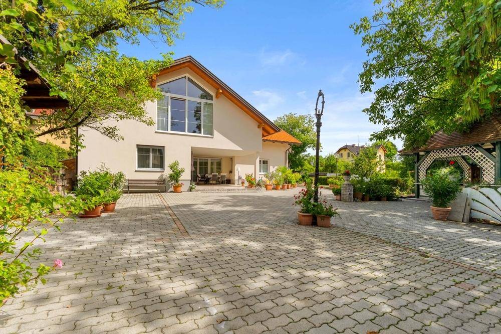 Großzügiges Einfamilienhaus mit weitläufiger gepflasterter Fläche und üppiger Begrünung im Garten.
