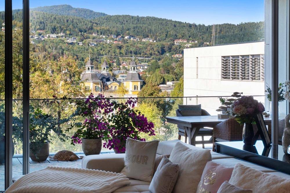 Gemütlicher Wohnbereich mit Sofa und weitem Blick auf die grüne Hügellandschaft und Gebäude.
