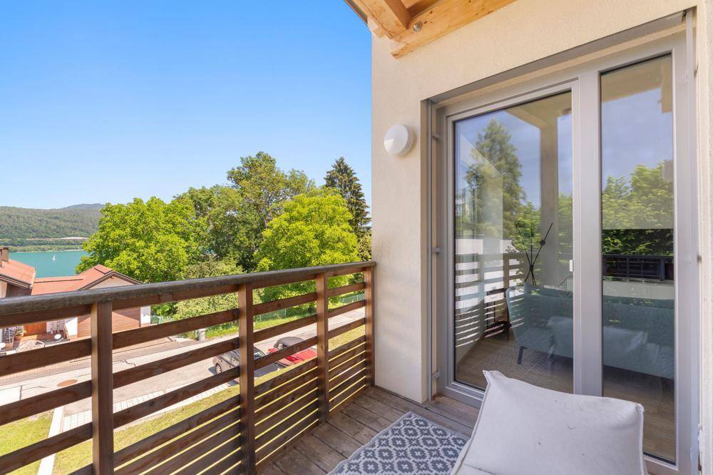 Sonniger Balkon mit Holzboden und Geländer, bietet einen schönen Blick auf den See.