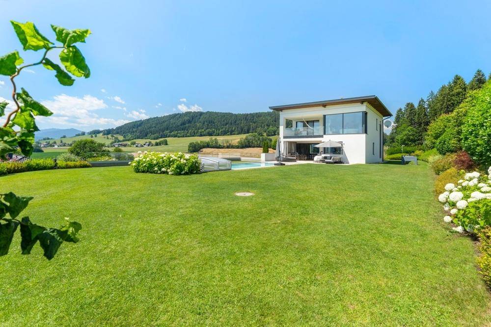Weitläufiger Gartenbereich mit gepflegtem Rasen und moderner Villa im Hintergrund, umgeben von Natur.