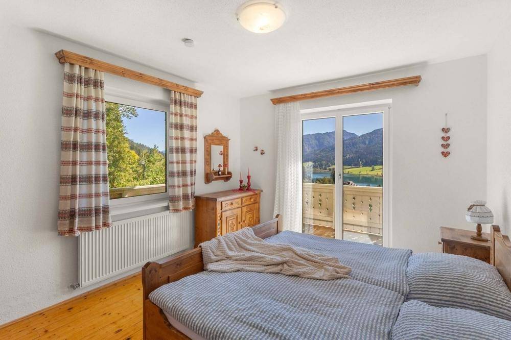 Schlafzimmer mit Holzboden und Balkonzugang, bietet einen malerischen Blick auf See und Berge.