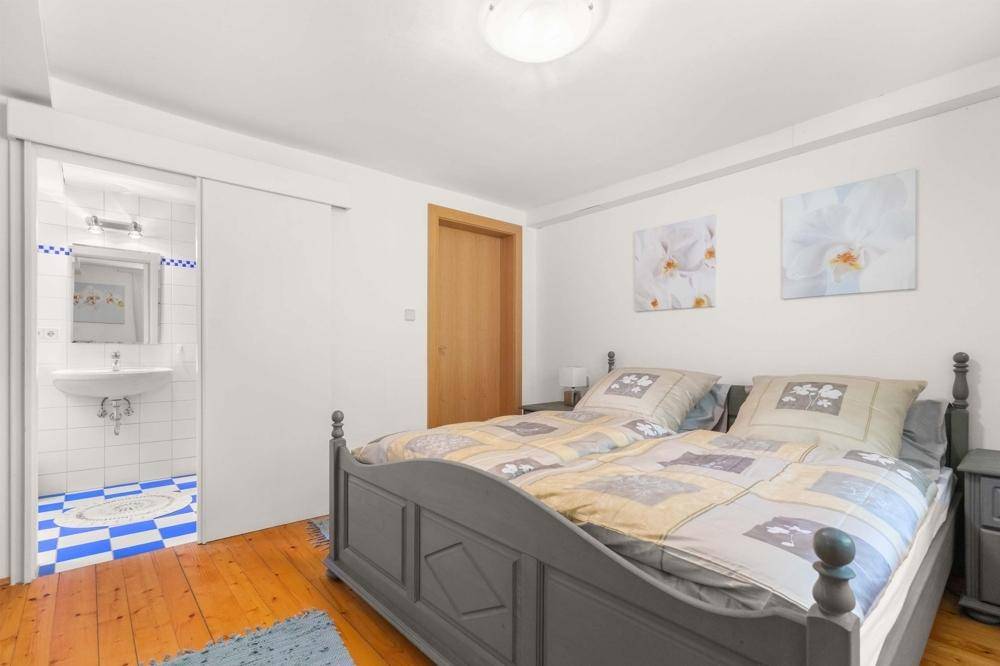 Schlafzimmer mit Holzboden und Doppelbett, angrenzendem Waschbereich mit Fliesenboden.