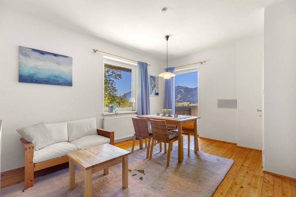 Gemütlicher Essbereich mit Holztisch und Stühlen, kleinem Sofa und Fenstern mit Bergblick.