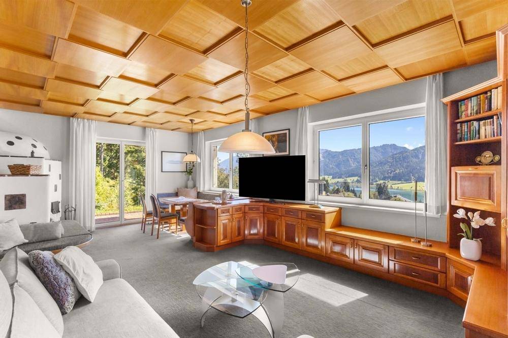 Geräumiges Wohnzimmer mit Holzkassettendecke, Einbaumöbeln und großem Fenster mit See- und Bergblick.