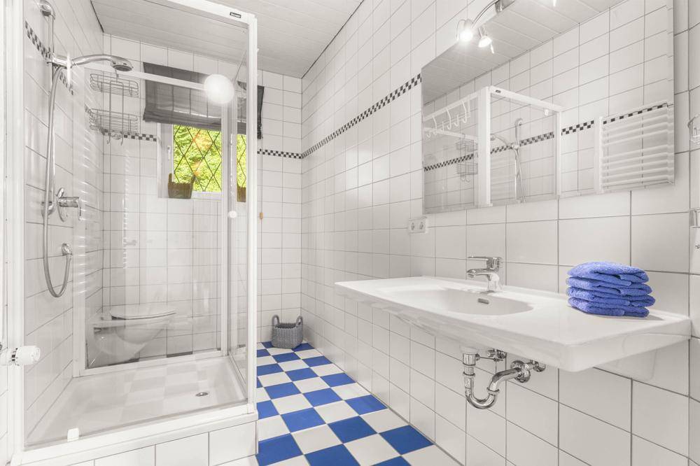 Helles Badezimmer mit weißen Fliesen, Duschkabine, Waschbecken und einem Fenster für Tageslicht.