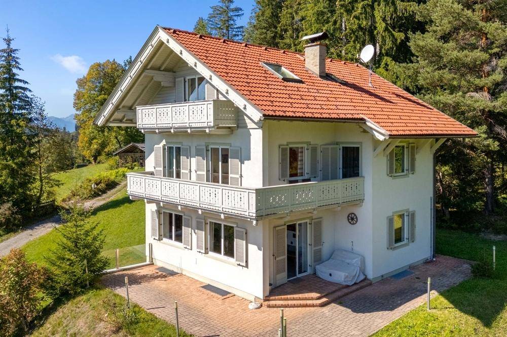 Charmantes weißes Haus mit traditionellem roten Dach, Balkonen und grünen Fensterläden, umgeben von Natur.
