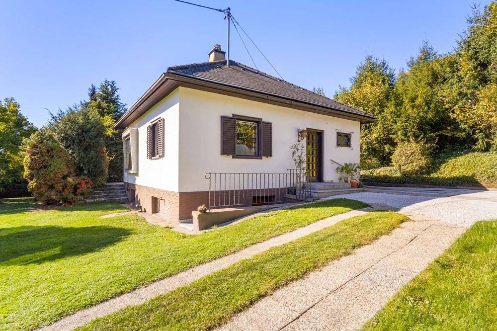 Das freistehende Haus mit Satteldach und Garten liegt in einer grünen Umgebung.