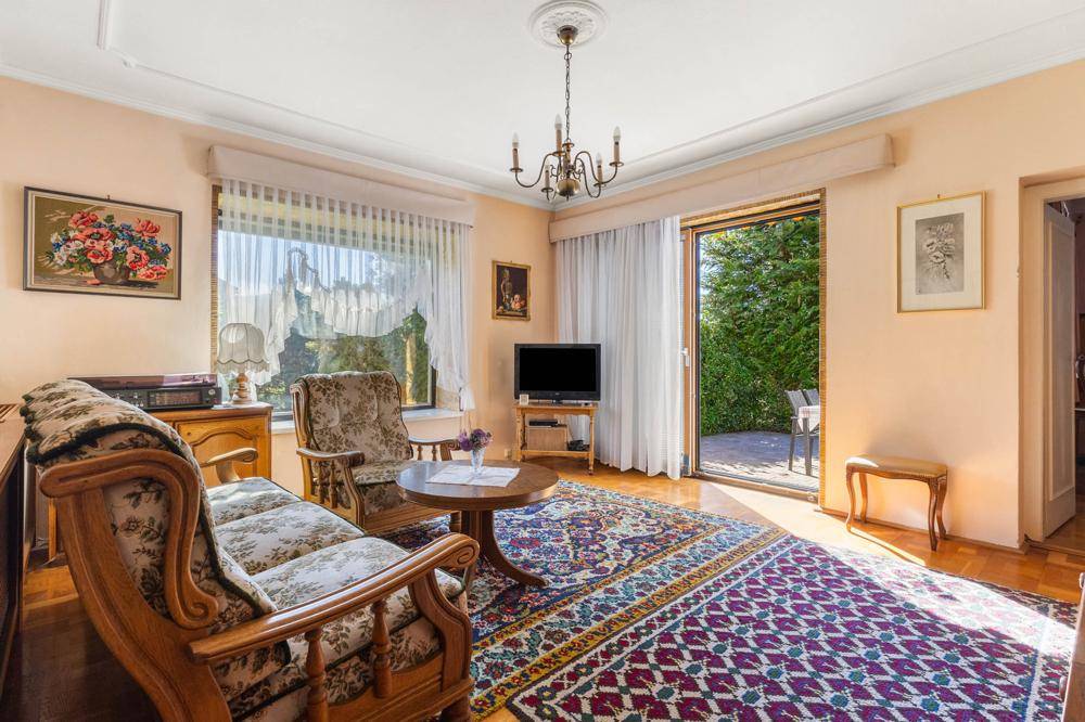 Helles Wohnzimmer mit Zugang zur Terrasse, Parkettboden und traditioneller Einrichtung.