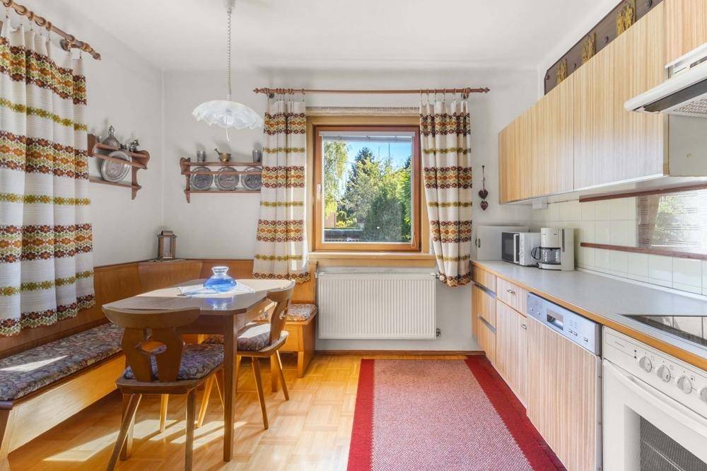 Gemütliche Wohnküche mit Holzeinbauten, Essecke und Blick ins Grüne durch das Fenster.