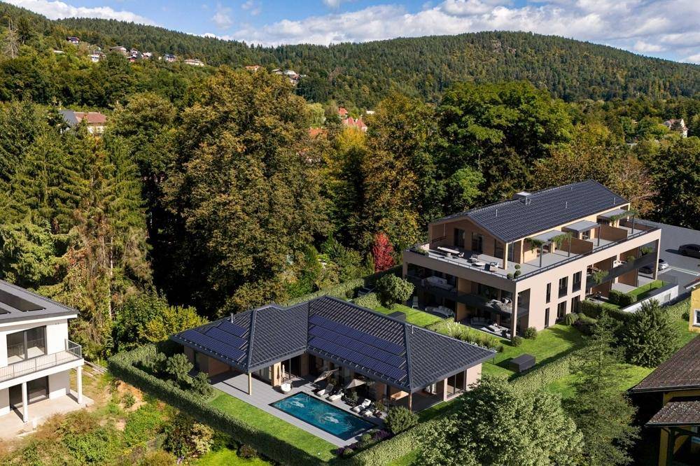 Luftaufnahme einer modernen Wohnanlage mit Pool und umgeben von viel Grün und Bergen.