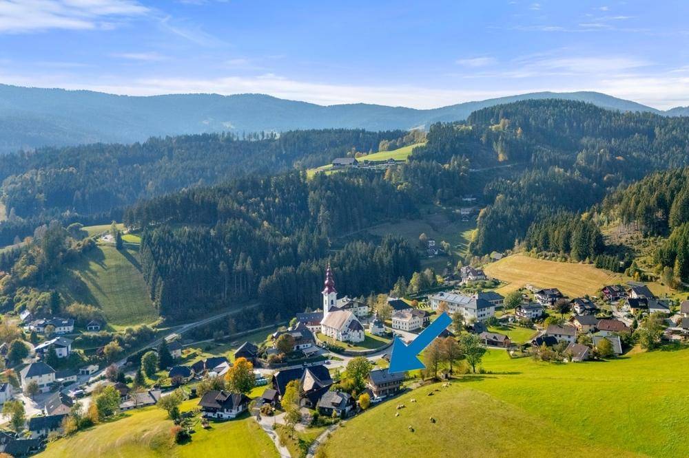 Luftaufnahme des Dorfes mit der Kirche und dem Anwesen, markiert durch einen blauen Pfeil.