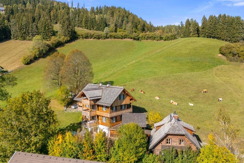 Traditionelles Holzhaus eingebettet in eine sanfte Hügellandschaft mit weidenden Kühen.