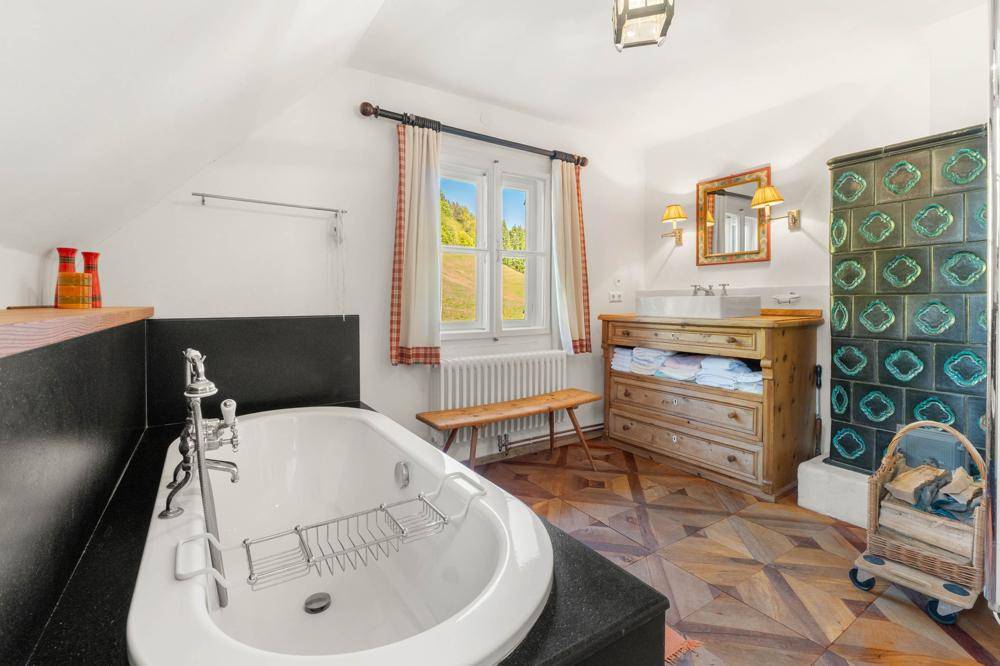 Helles Badezimmer im Dachgeschoss mit Badewanne, Kachelofen und Holzboden.