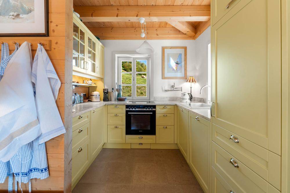 Helle Küche im Landhausstil mit gelben Schränken, Backofen und Blick ins Grüne.