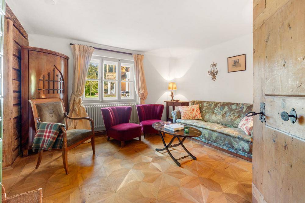 Gemütliches Wohnzimmer mit Parkettboden, floralem Sofa und zwei roten Sesseln.