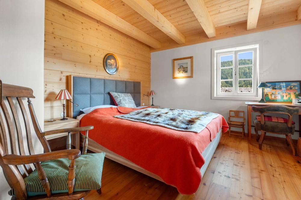 Gemütliches Schlafzimmer mit Holzwänden, Holzbalkendecke und Blick auf die Berge.