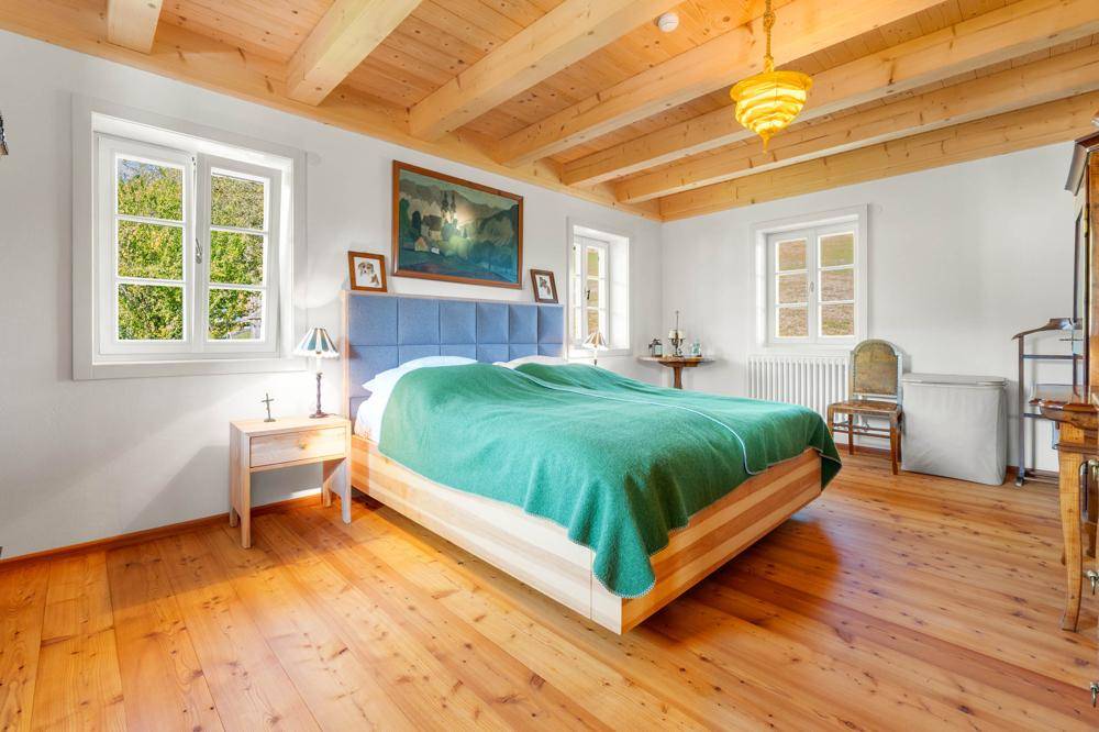 Helles Schlafzimmer mit Holzbalkendecke, Holzboden und einem großen Doppelbett.