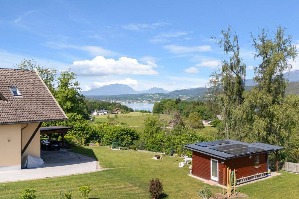 Gepflegter Gartenbereich mit Rasen, einem kleinen Schuppen mit Solaranlage und weitem Blick auf den See und die Berge.
