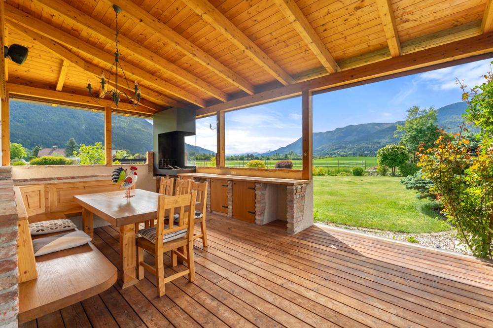 Überdachte Terrasse mit Holzboden, Essbereich und integriertem Grill mit Bergblick.