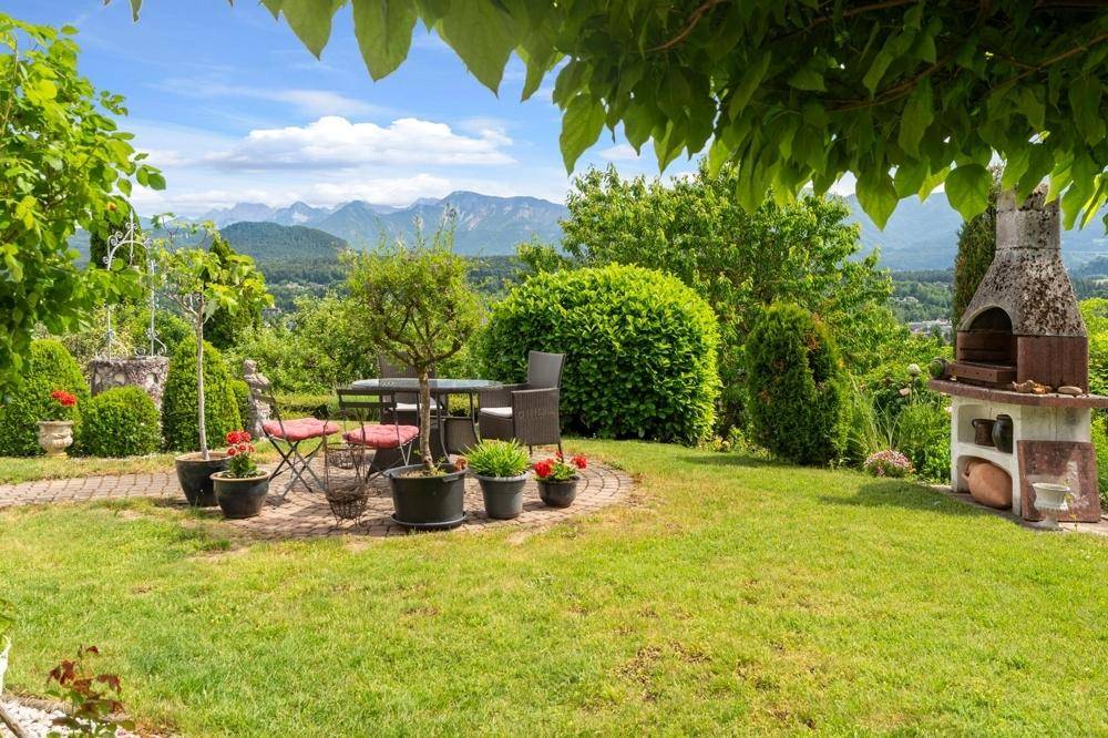 Gepflegter Garten mit Sitzgelegenheiten und Grillplatz, umgeben von grüner Natur und Bergblick.
