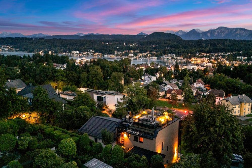 Luftaufnahme des Anwesens bei Sonnenuntergang, mit beleuchteter Dachterrasse und malerischer Umgebung.