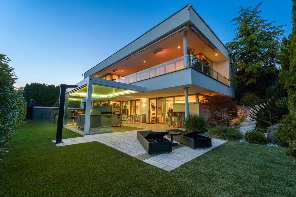 Elegante moderne Villa mit weitläufigem Garten, gepflasterter Terrasse und überdachter Außenküche.