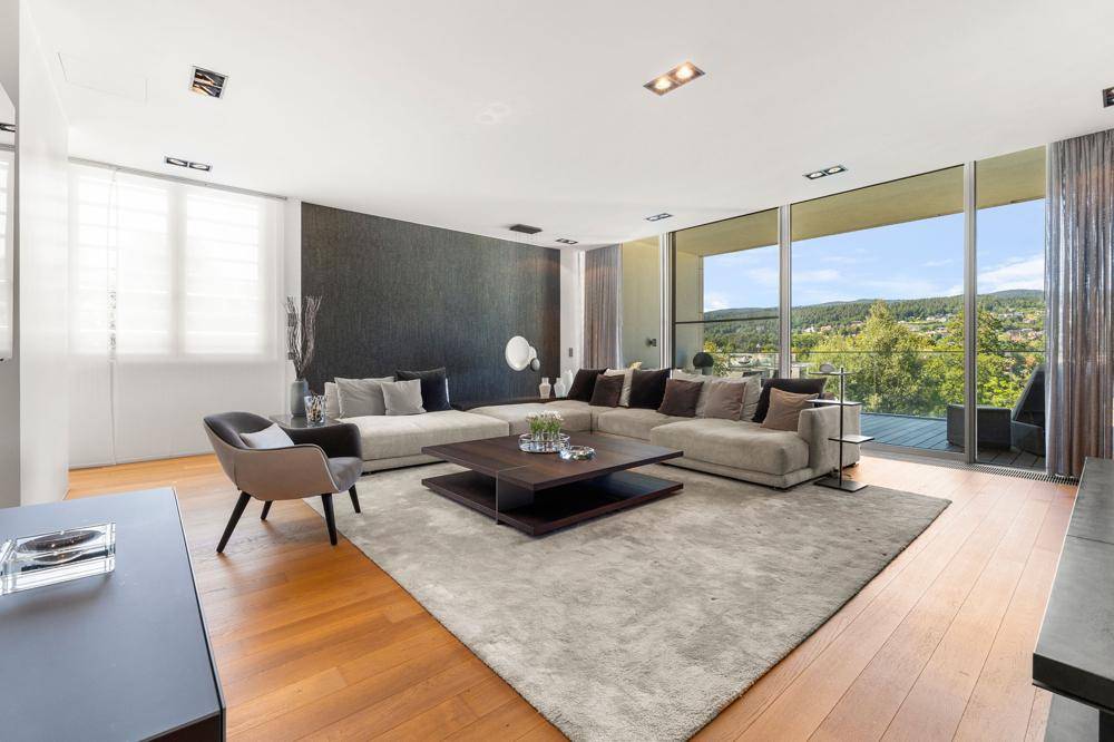 Geräumiges Wohnzimmer mit großem Sofa, Holzboden und raumhohen Fenstern mit Weitblick ins Grüne.