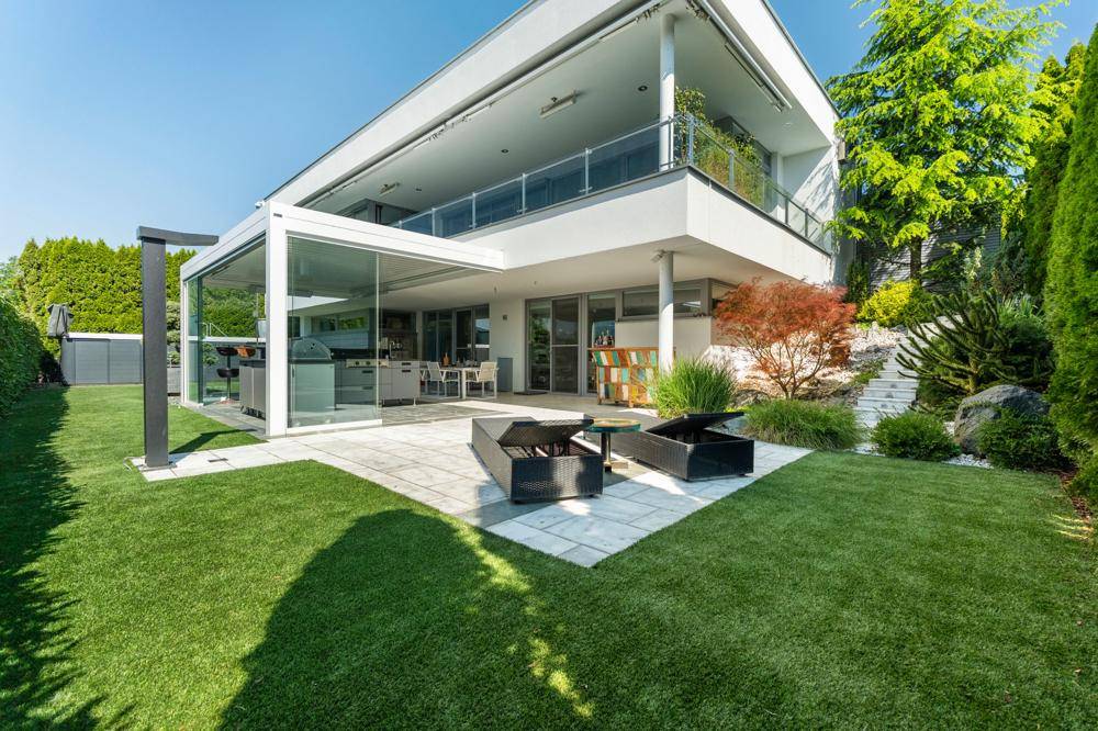 Zeitgenössische Villa mit gepflegtem Rasen, sonniger Terrasse und einer stilvollen überdachten Außenküche.