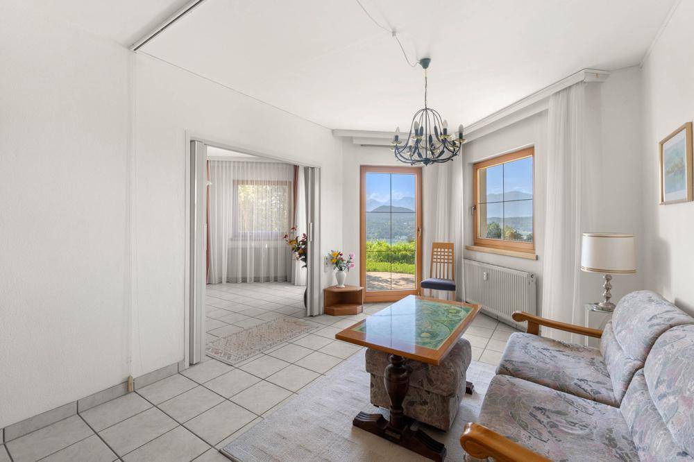Gemütliches Wohnzimmer mit Fliesenboden, Sofa und einem großen Fenster mit Seeblick.