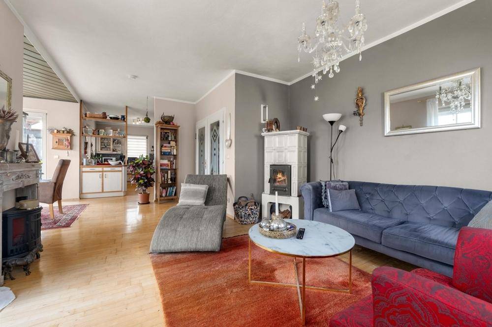 Gemütliches Wohnzimmer mit Kachelofen, Sofa und Blick in den offenen Küchenbereich.