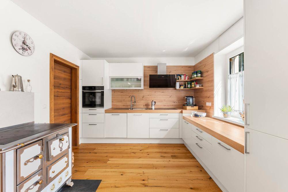 Funktionale Küche mit weißen Fronten, Holzarbeitsplatten und einem Fenster für natürliches Licht.