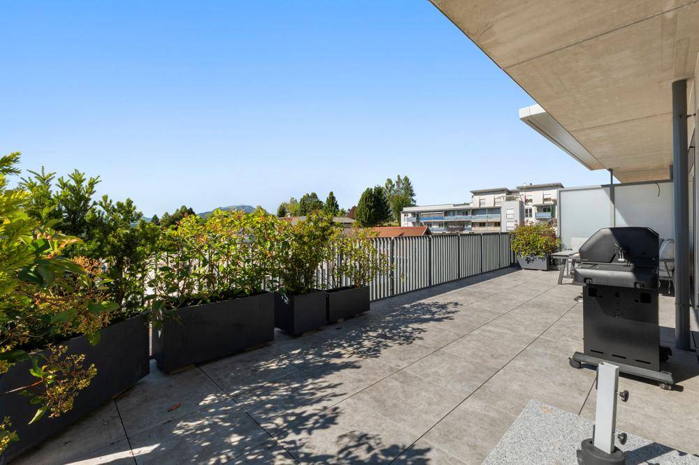 Weitläufige Terrasse mit Fliesenboden, Grill und dekorativen Pflanzen in langen Kübeln.