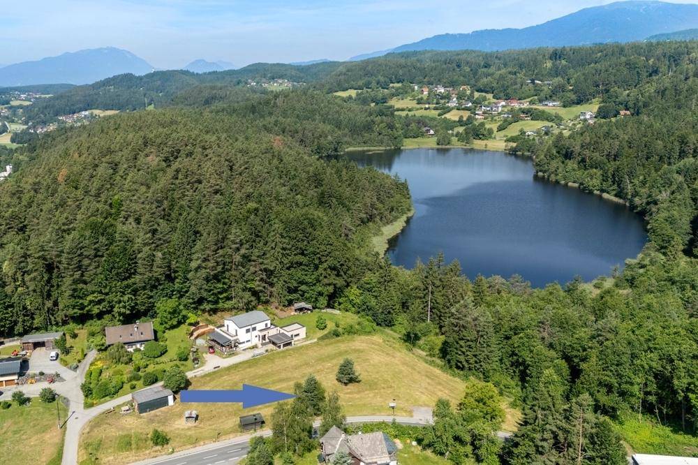 Luftaufnahme einer Wohngegend am Waldrand mit Blick auf einen kleinen See.