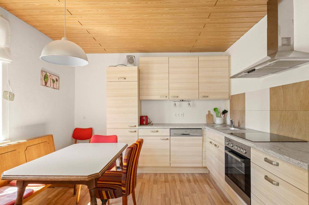 Gemütliche Küche mit hellen Holzschränken, Esstisch und einer Holzdecke.