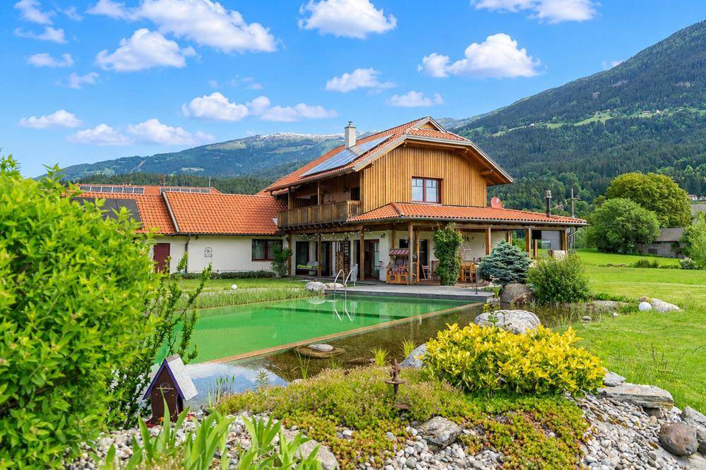 Idyllischer Gartenbereich mit Naturpool, Teich und traditionellem Haus vor Bergkulisse.